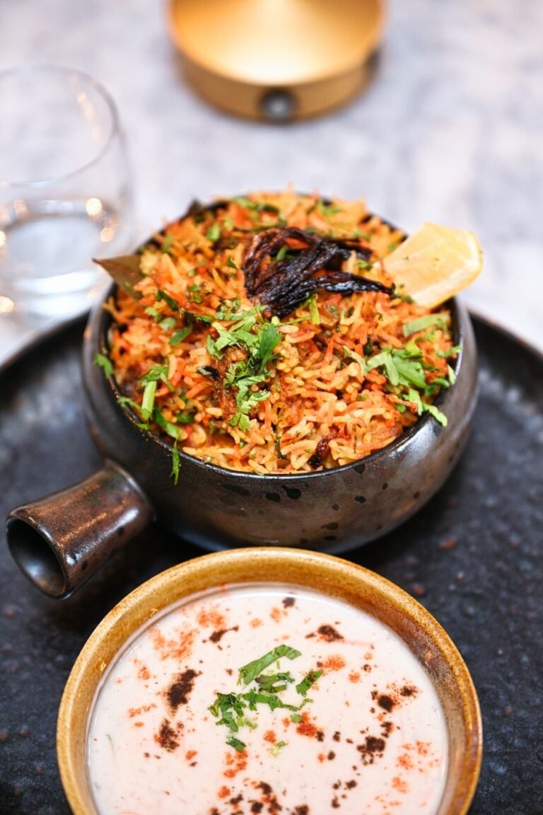 Chicken biryani served in a pot with a bowl of raita