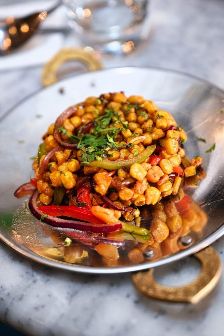A tower of chickpea chaat with tomato, onion and coriander on a silver plate