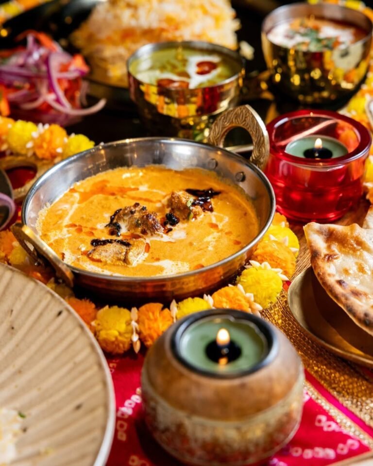 A rich makhani curry in a copper kadai, surrounded by marigolds and candles
